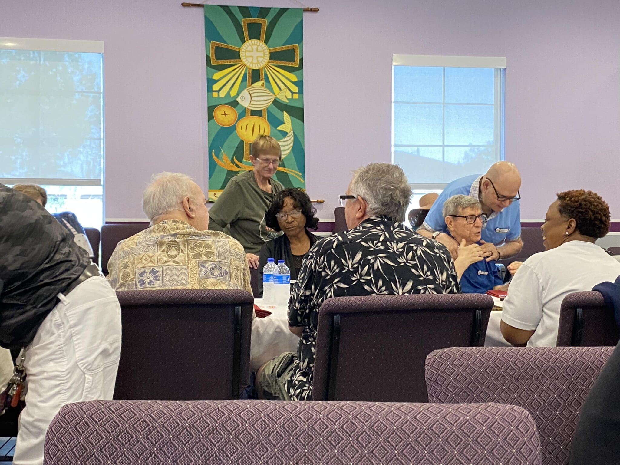 A group of elderly people engaged in conversation in a community room.