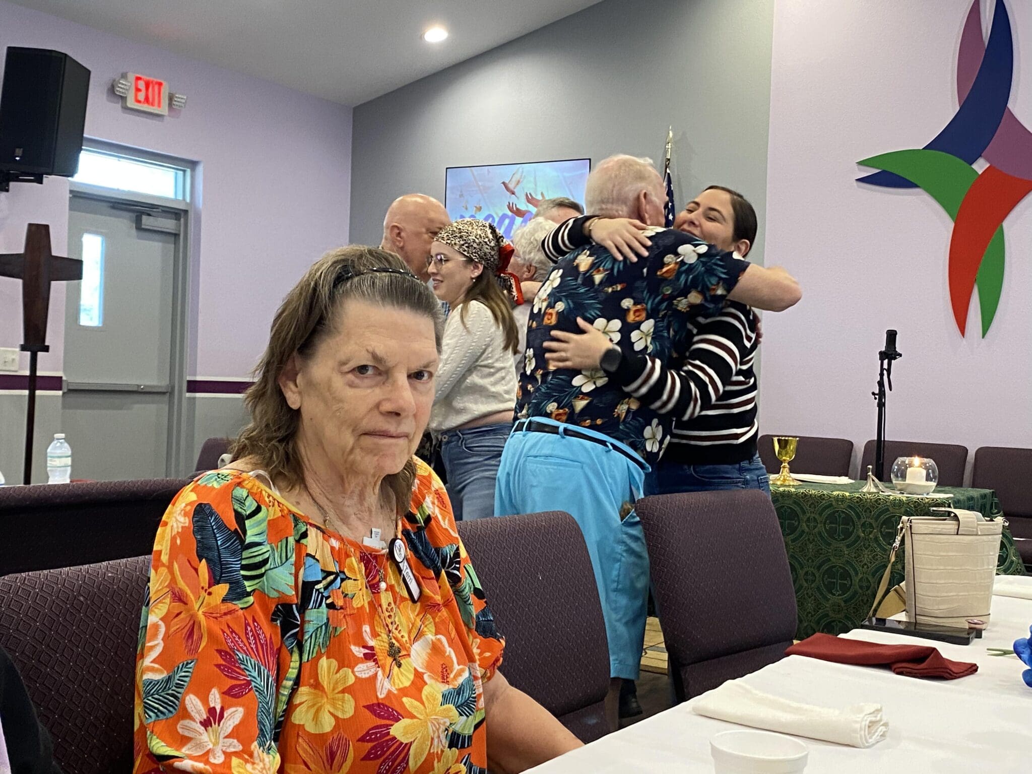 Elderly woman sitting at a table with two children on a woman's lap behind her.