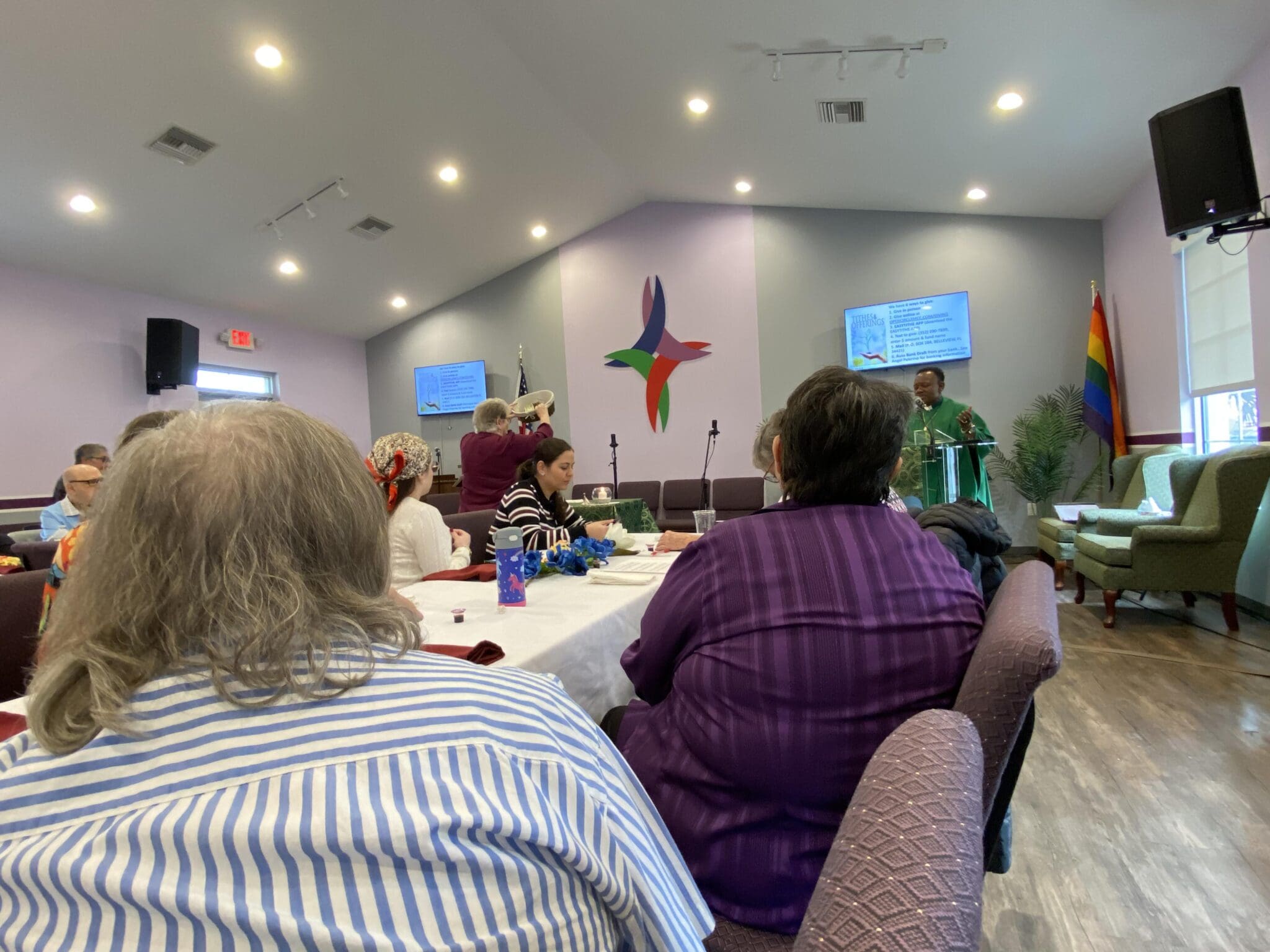 People attending a church service with a cross and a speaker at the front.