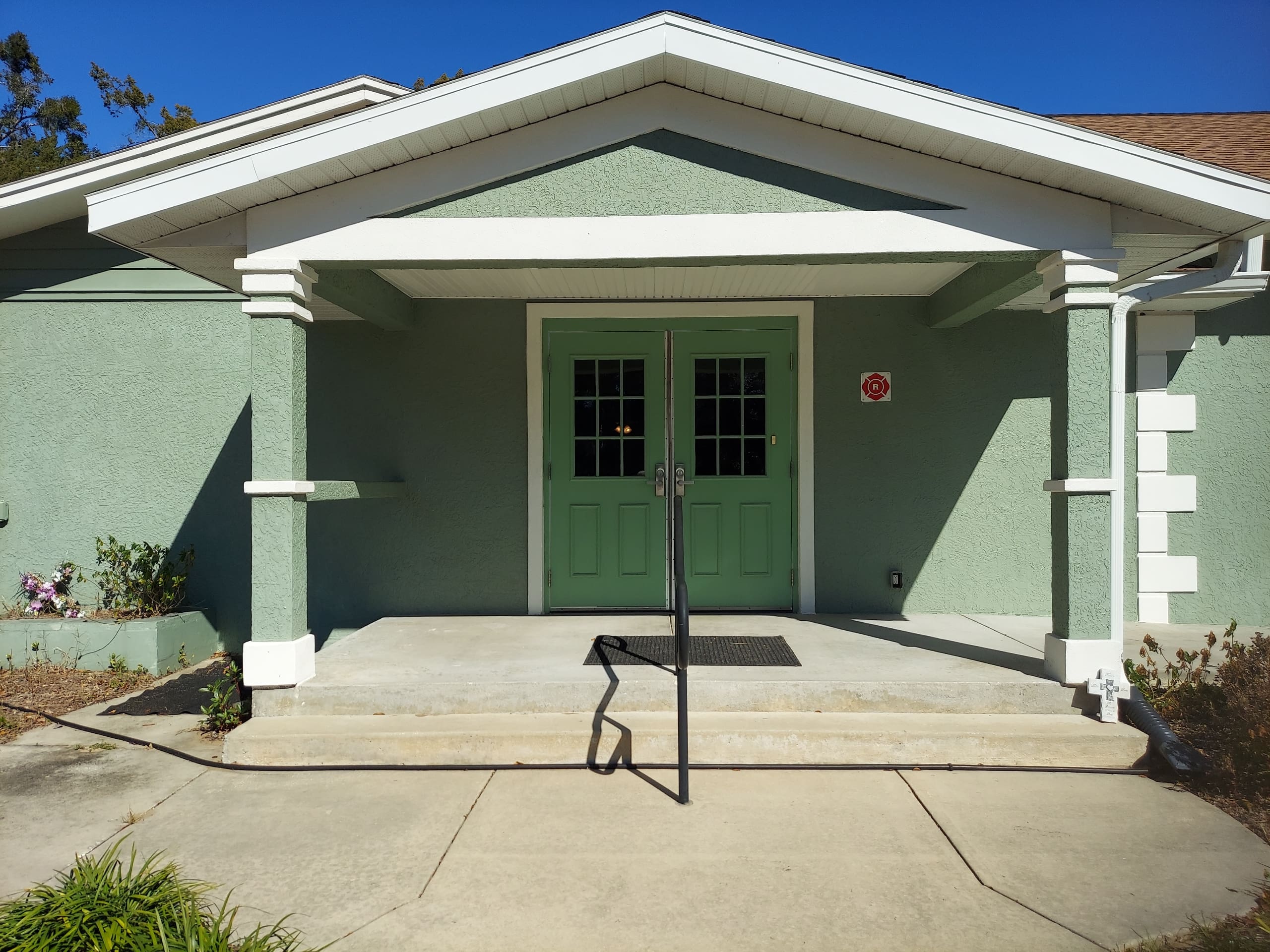 Green building entrance with double doors and a handrail.