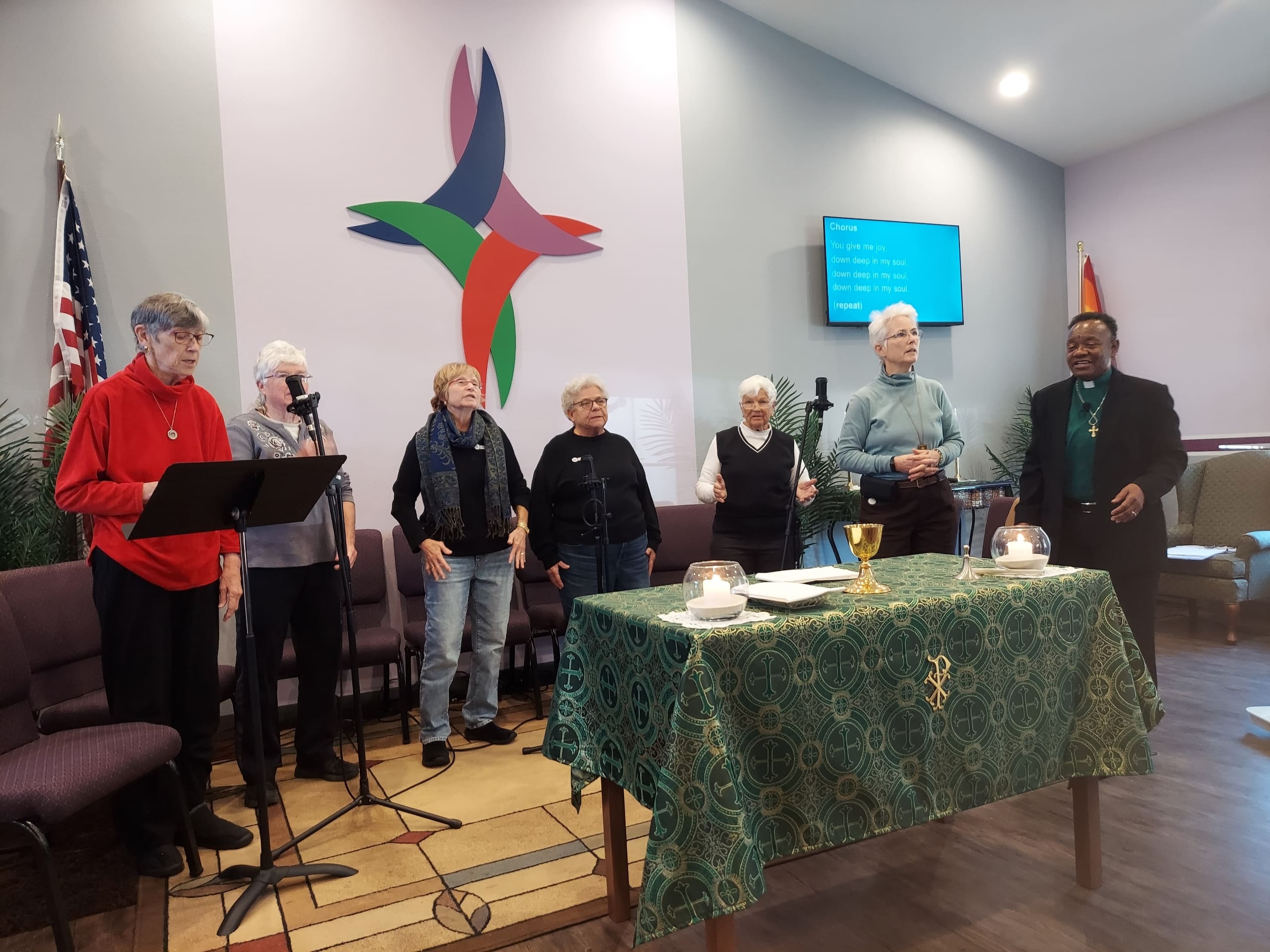 Group of people standing by a decorated table in a room with a colorful wall design.