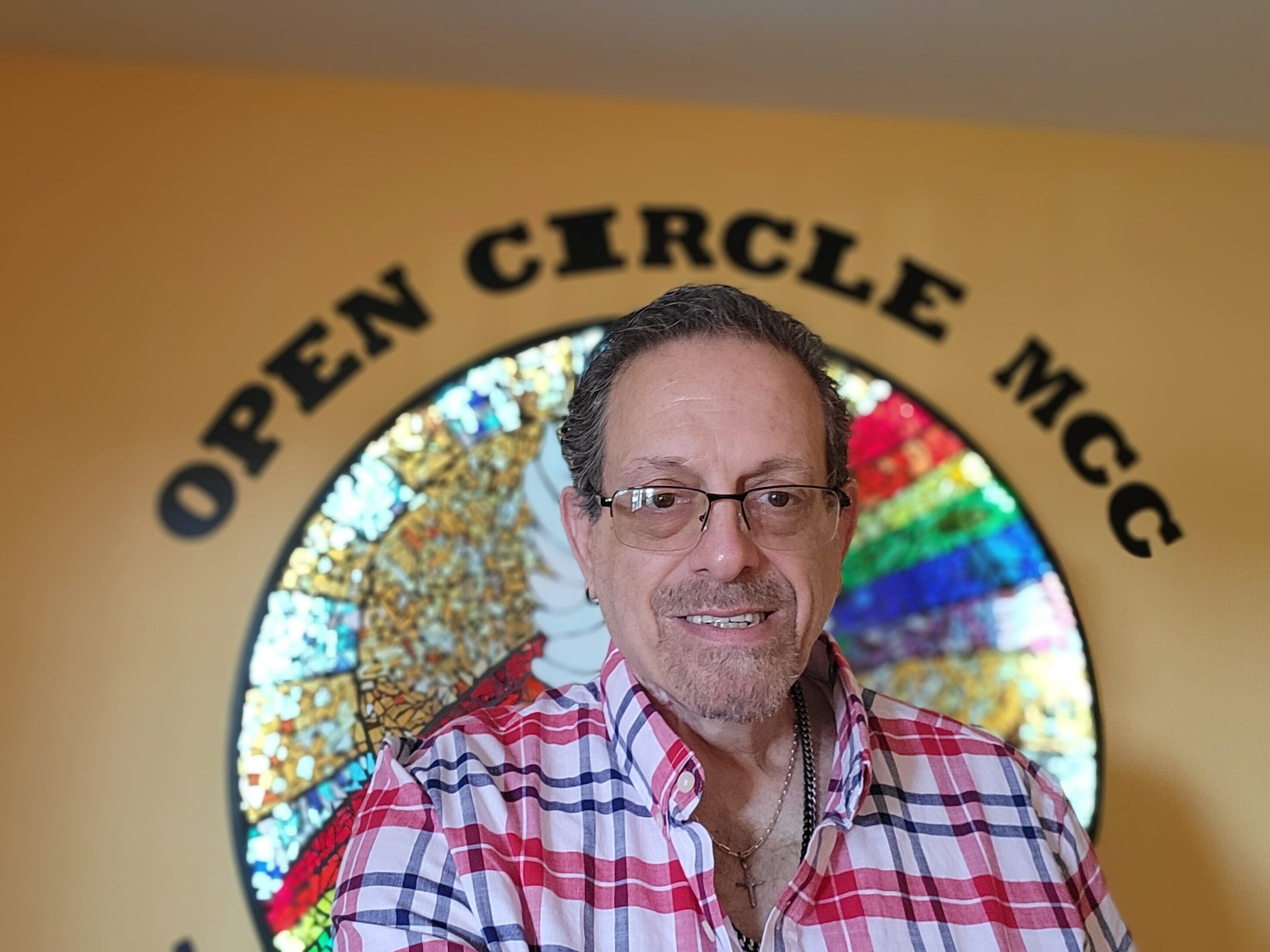 Man smiling in front of a colorful circular stained glass window.