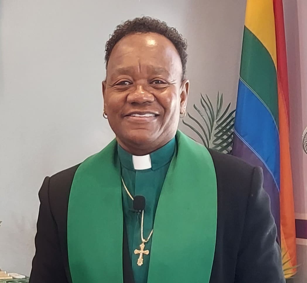 Smiling clergyman wearing green stole and cross necklace.