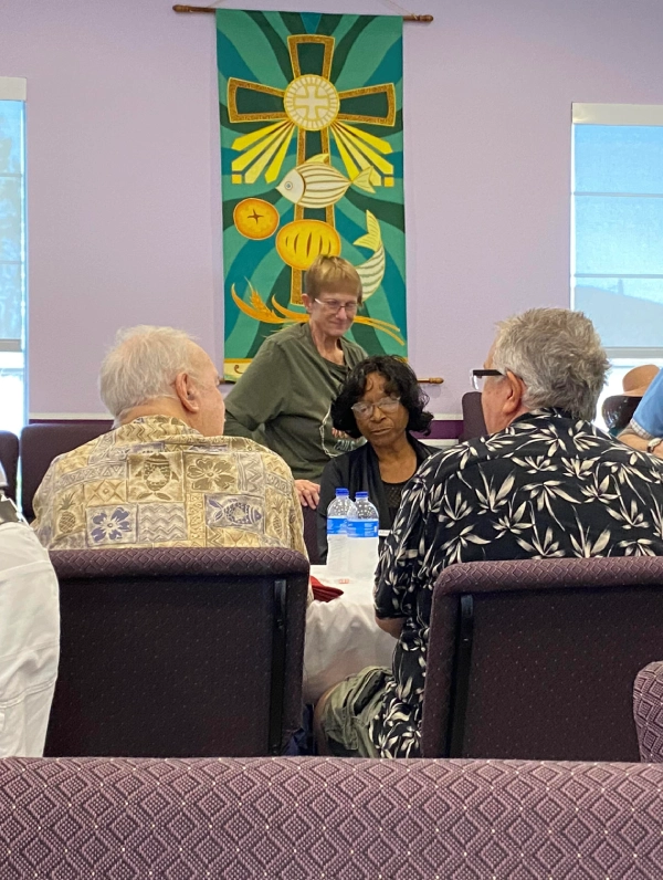 A woman speaks to an audience seated at tables with colorful decorations.