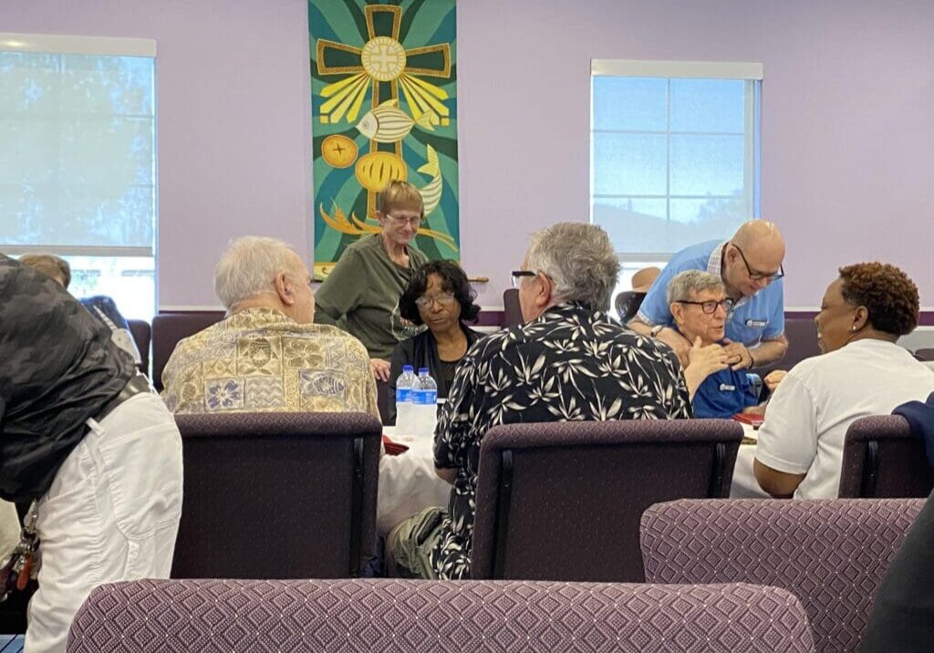 A group of elderly people engaged in conversation in a community room.