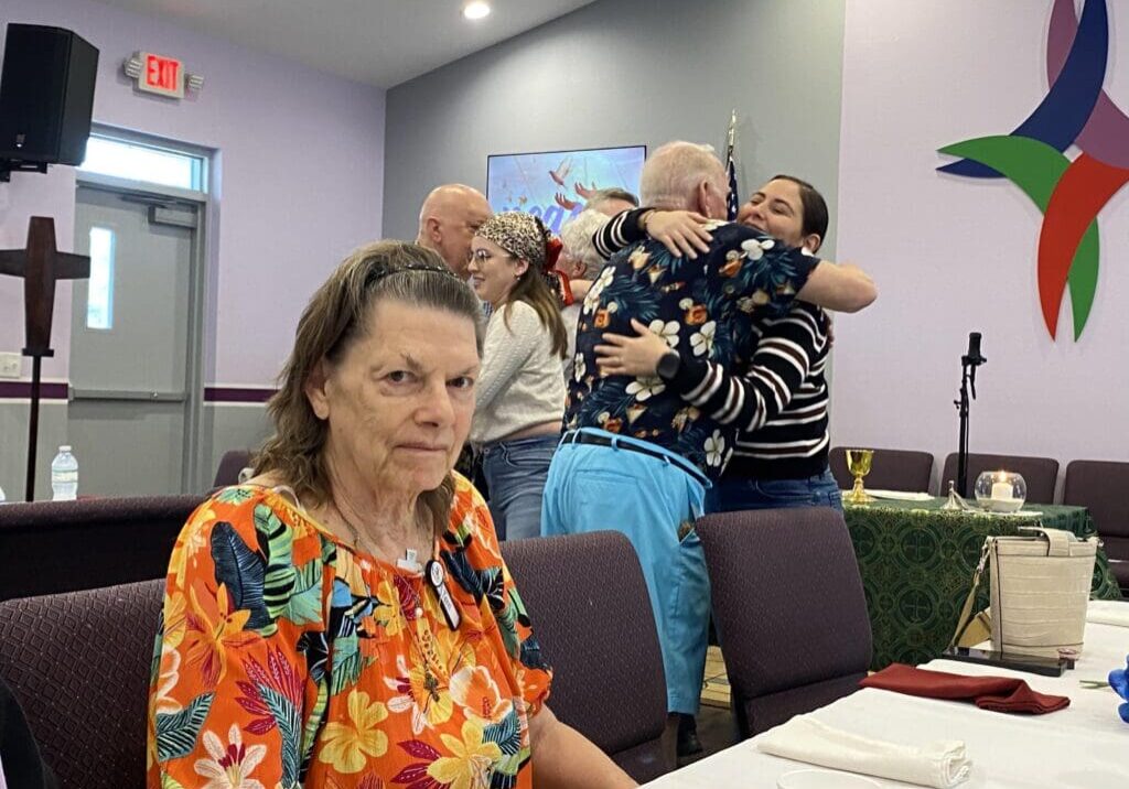 Elderly woman sitting at a table with two children on a woman's lap behind her.