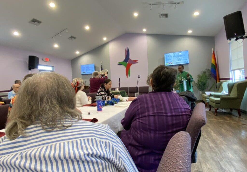 People attending a church service with a cross and a speaker at the front.