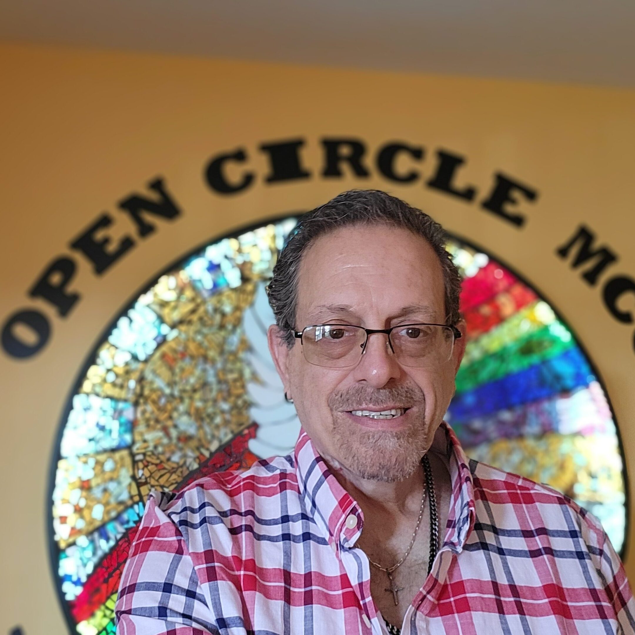 Man in glasses and plaid shirt standing in front of a colorful circular window.