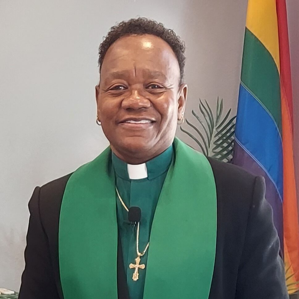 Smiling clergyman wearing green stole and cross necklace.