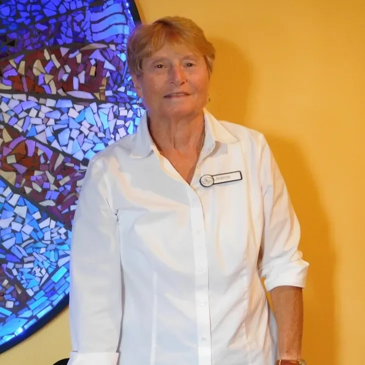Woman in white shirt stands near stained glass window.
